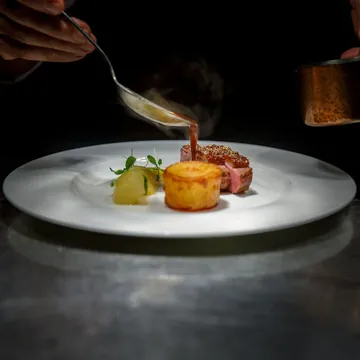 A chef spooning sauce over a plated steak